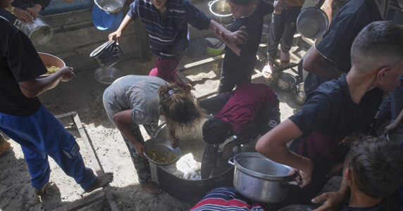 Två barn skrapar det sista från botten i en stor gryta.