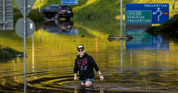 En man i keps och solglasögon vadar fram på en översvämmad väg.