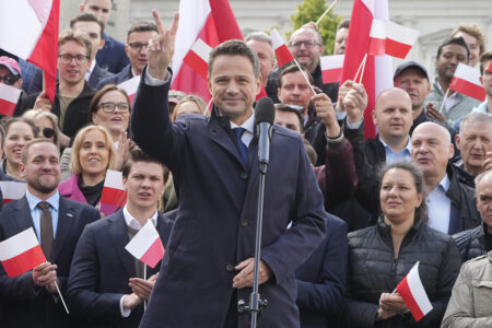 Polens liberala presidentkandidat Rafal Trzaskowski står framför folksamling med flaggor, gör segertecknet