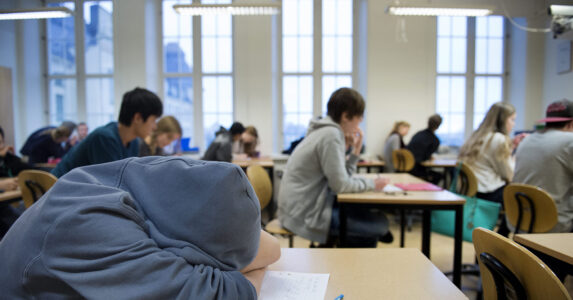 Tonåringar i ett klassrum. En sover lutad över bänken.