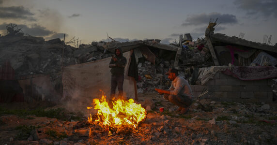 Två män vid en eld bland ruiner.