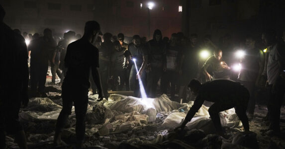 Människor som lyser med ficklampor i mörkret på svepta kroppar som ligger på marken.