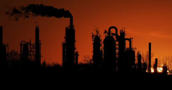 Ett oljeraffinaderi i siluett mot röd solnedgång.
