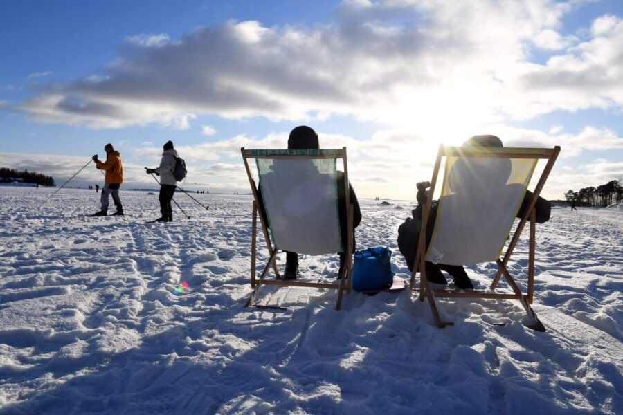 Folk skidar, sitter i solstolar i vintersolen