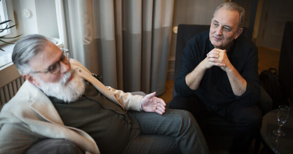 Två gråhåriga män sitter vid ett fönster.