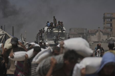 Män bär på säckar med nödhjälp, från en lastbil som syns i bakgrunden, full med människor som klättrat upp på den.