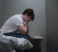 En kille sitter på sängen med huvudet i händerna.