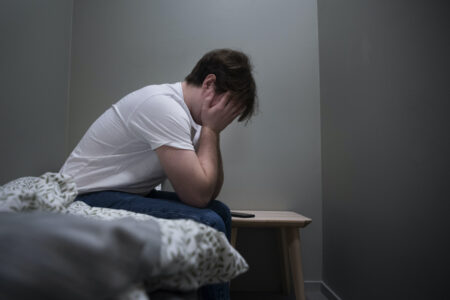 En kille sitter på sängen med huvudet i händerna.