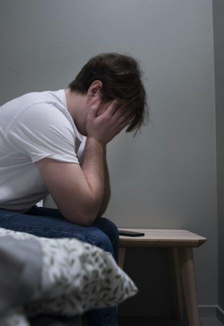 En kille sitter på sängen med huvudet i händerna.