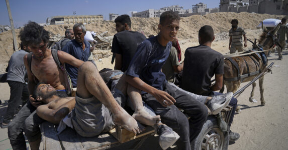 En skadad man körs på en vagn efter en åsna i ett ruinlandskap.