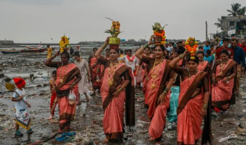 Några kvinnor tar sig fram genom en strand fylld med plastavfall för att offra kokosnötter till havet för att fira Narali Pournima, eller kokosnötsfestivalen, i Mumbai, Indien, måndagen den 19 augusti 2024. (AP Photo/Rafiq Maqbool)