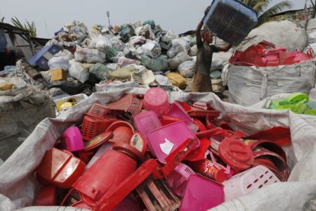 En man står på ett plastberg och arbetar med att sortera plast.