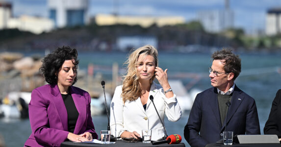Tre personer framför en vik med ett kärnkraftverk på andra sidan.