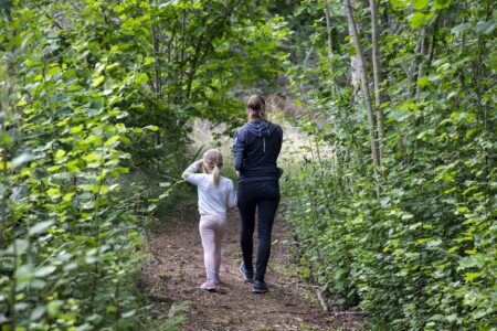En mor och dotter promenerar på en skogsstig.
