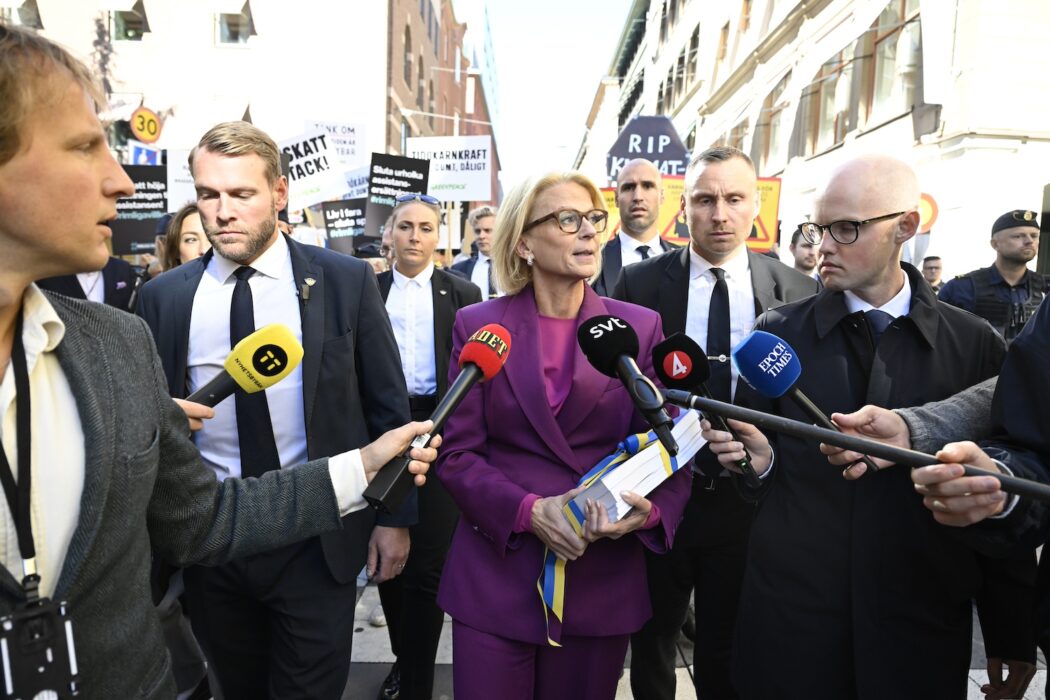 Finansminister Elisabeth Svantesson promenerar med budgeten, omgiven av säkerhetsvakter och journalister.