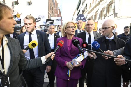 Finansminister Elisabeth Svantesson promenerar med budgeten, omgiven av säkerhetsvakter och journalister.