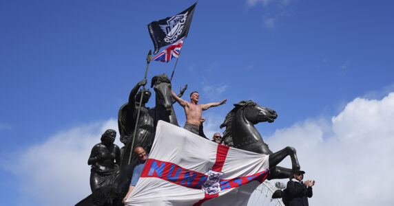 En man med bar överkropp på en staty med Englands flagga.