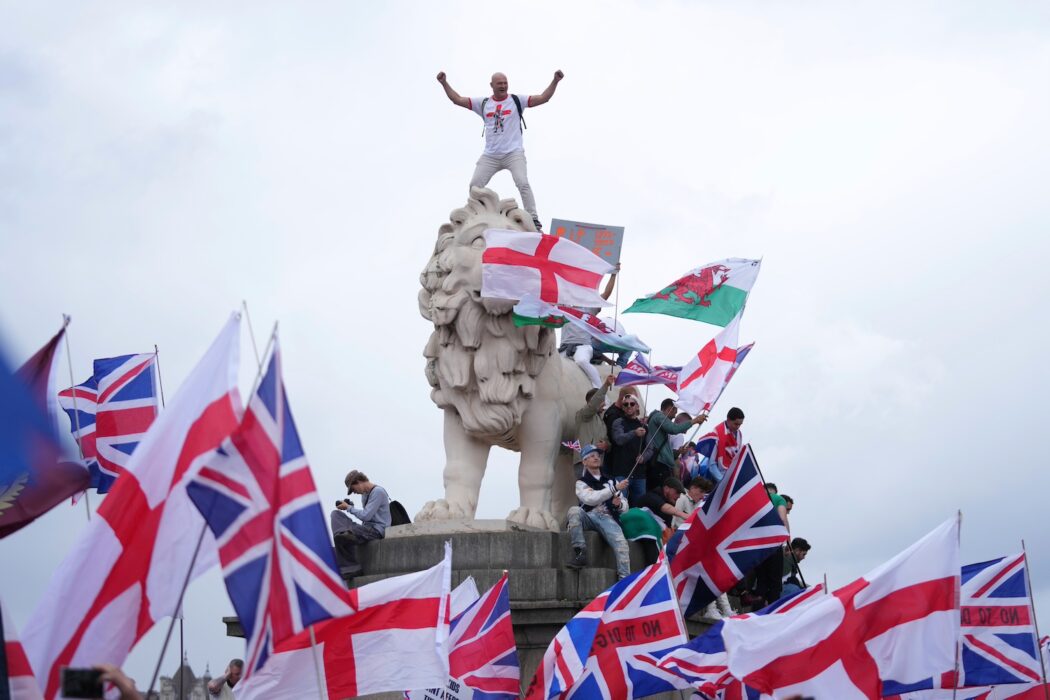 Demonstranter med engelska och brittiska flaggan står runt och på en staty.