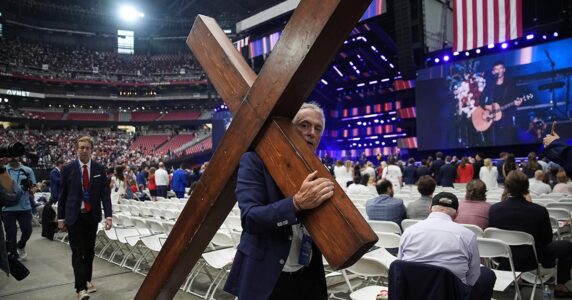 En man drar ett stort träkors över golvet.