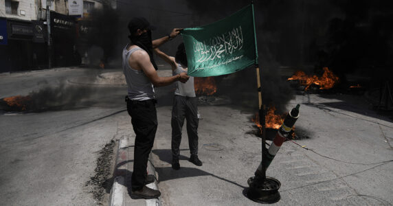 Två unga maskerade män med en Hamas-flagga och en låtsasraket.