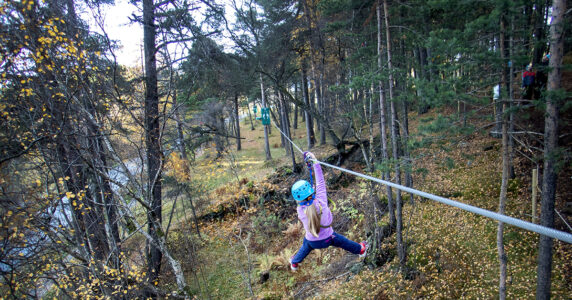 Ett barn åker linbana bland trädtopparna.