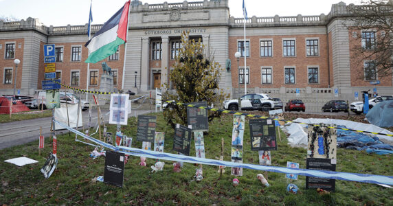 En byggnad med plakat och grejer utanför och avspärrningsband framför.
