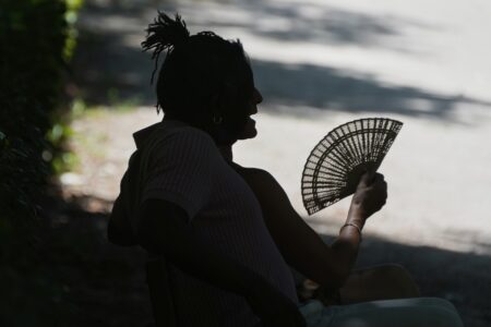 En person sitter i skuggan med en solfjäder.