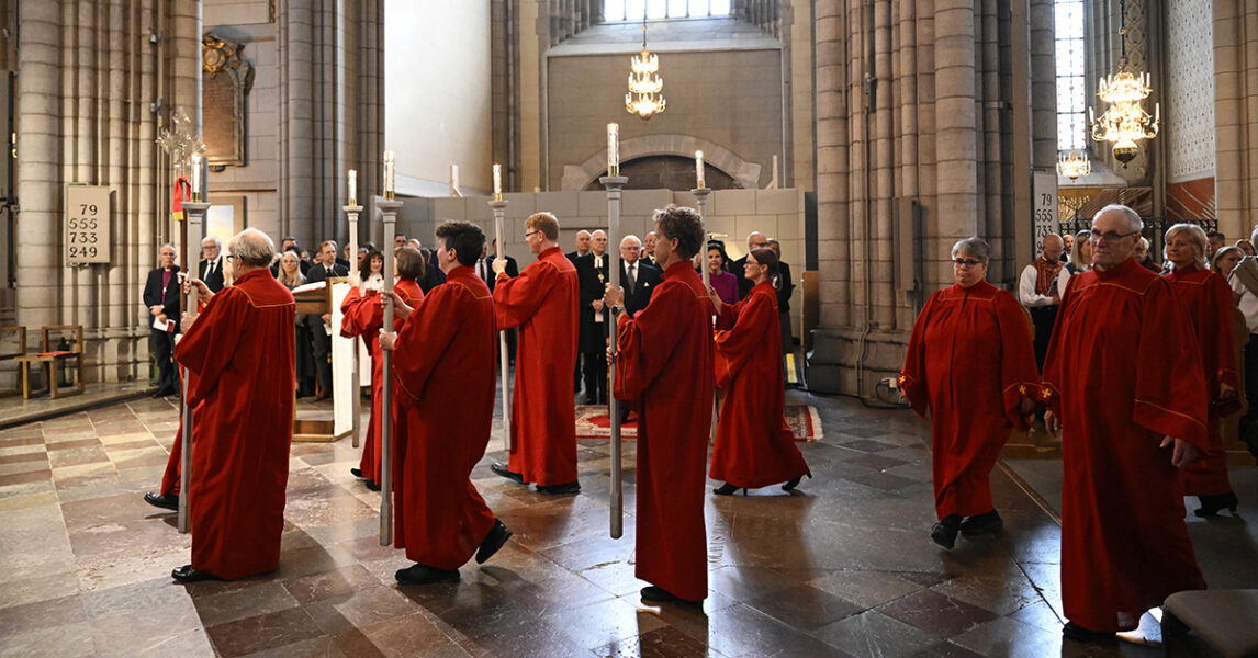 Människor i röda mantlar under en ceremoni i en kyrka.