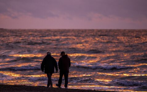 Två personer promenerar längs en strand längs Östersjön.