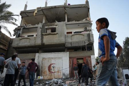 Hus med demolerad fasad, människor inspekterar förödelsen, ett barn i förgrunden