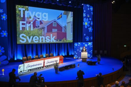 Jimmie Åkesson på scenen, framför en skärm med orden "Trygg, fri, svensk".