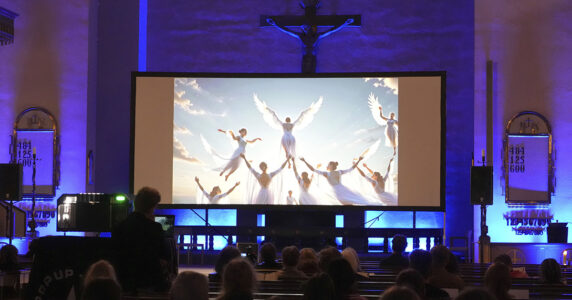 Gudstjänst i en kyrka med en skärm med änglar.