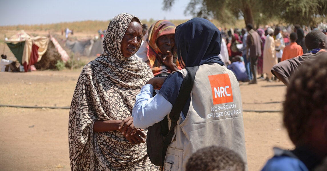 Två kvinnor pratar, den ena har en väst från Norska flyktingrådet.