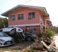 Skyfall och översvämning i Thailand. Bil ligger ovanpå en annan bil invid en gata och ett hus.