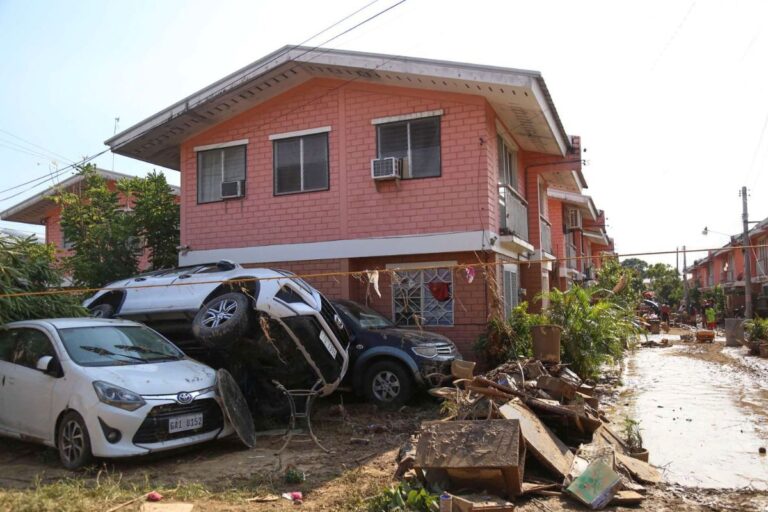 Skyfall och översvämning i Thailand. Bil ligger ovanpå en annan bil invid en gata och ett hus.