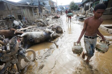 En man bär vattendunkar längs med en gyttjig gata kantad av döda djurkadaver.
