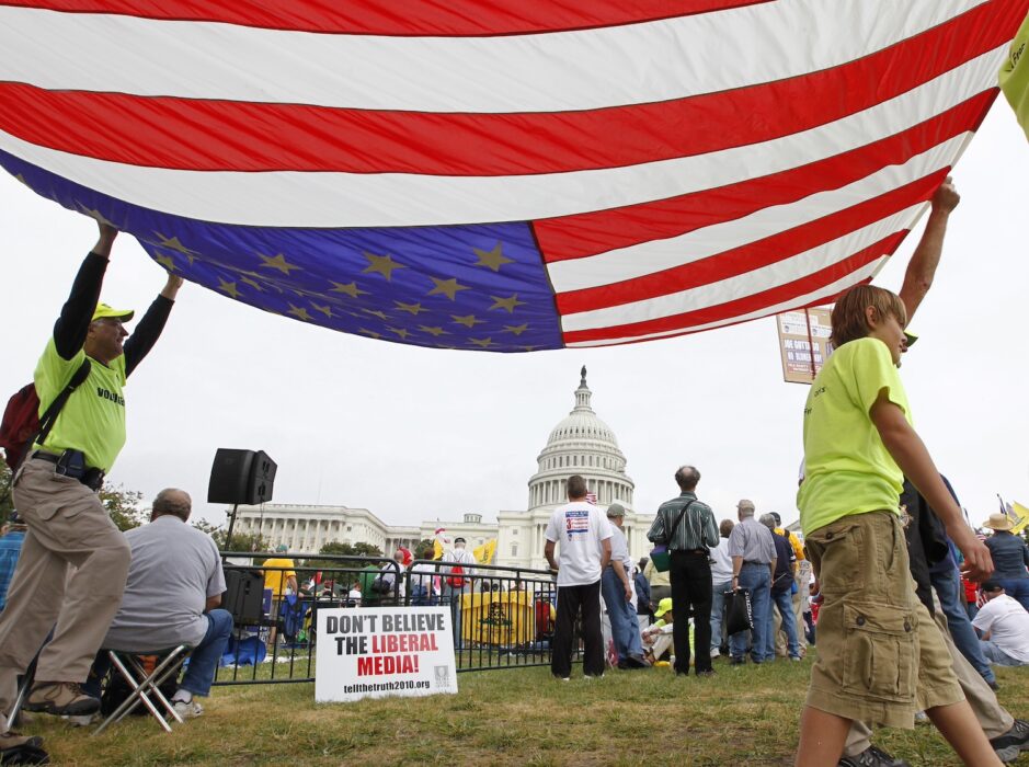 Demonstranter håller en stor USA-flagga framför vita huset.