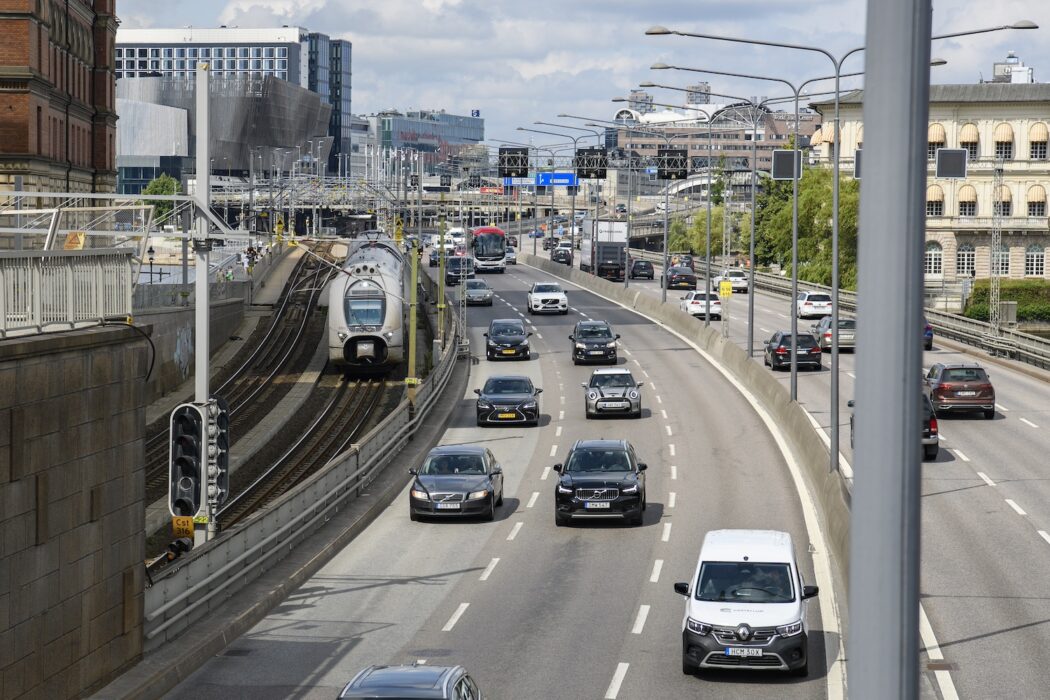 Trafik på en motorväg i stockholm, som går parallellt med ett tågspår.