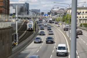 Trafik på en motorväg i stockholm, som går parallellt med ett tågspår.