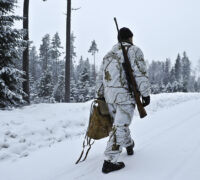 jägare går bort från kameran, gevär på axeln, vinterlandskap