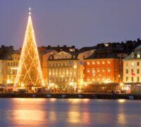 Lysande julgran framför hus längs vattnet i Gamla stan