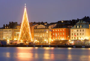 Lysande julgran framför hus längs vattnet i Gamla stan
