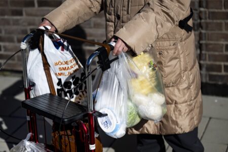 En pensionär med rullator bär matkassar.