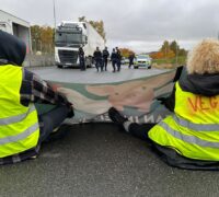 Två aktivister sitter ned och blockerar vägen för en lastbil.