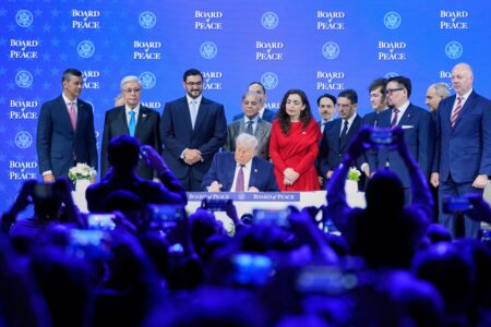 Donald Trump undertecknar ett dokument på scenen, med flera landsrepresentanter omkring sig.