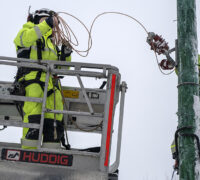 Två reparatörer lagar elledningar i snöig skog.