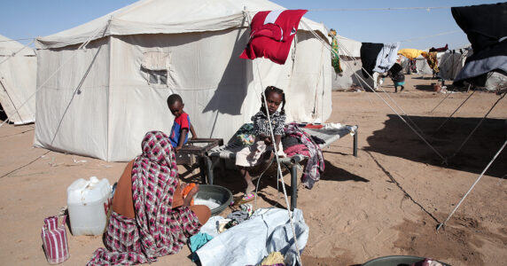 En kvinna tvättar och två barn tittar på utanför ett tält i en öken.