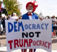 En man håller upp en skylt med texten: Democracy, nor Trumpocracy.