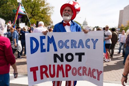 En man håller upp en skylt med texten: Democracy, nor Trumpocracy.