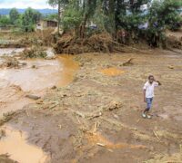 En pojke står i ett lerigt område förstört av en översvämning.